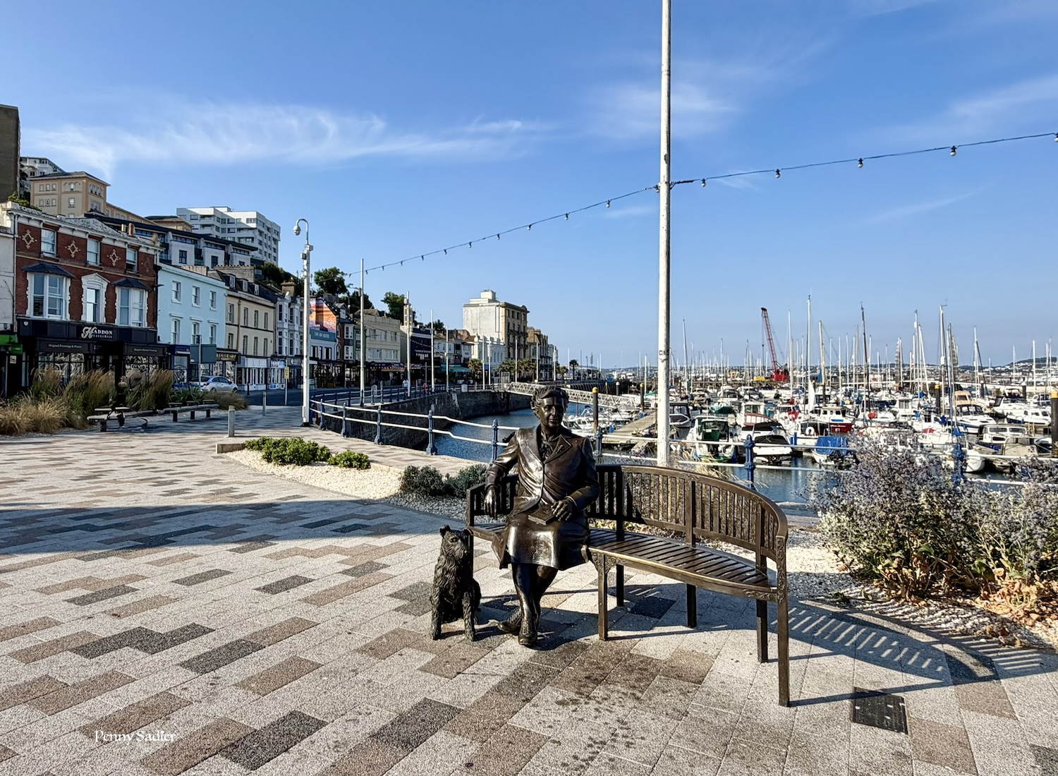 Sculpture of Agatha Christie seated with her dog in front of the Torquay harbor, Devon, England.