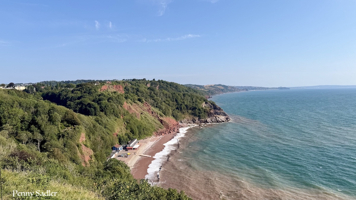 Oddicombe Beach viewed from the Downs, showing turquoise water and the red sandstone cliffs of the English Riviera in Devon.