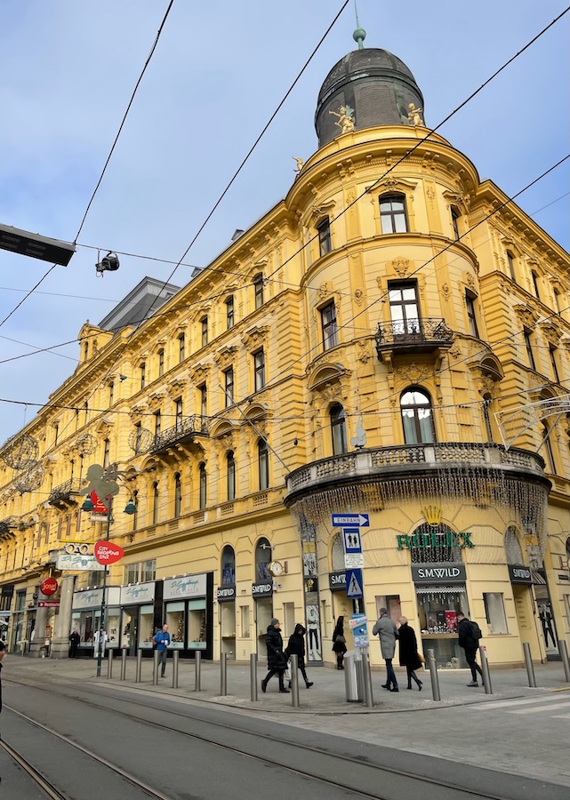Historic yellow building in central Linz, Austria with tram lines and street life