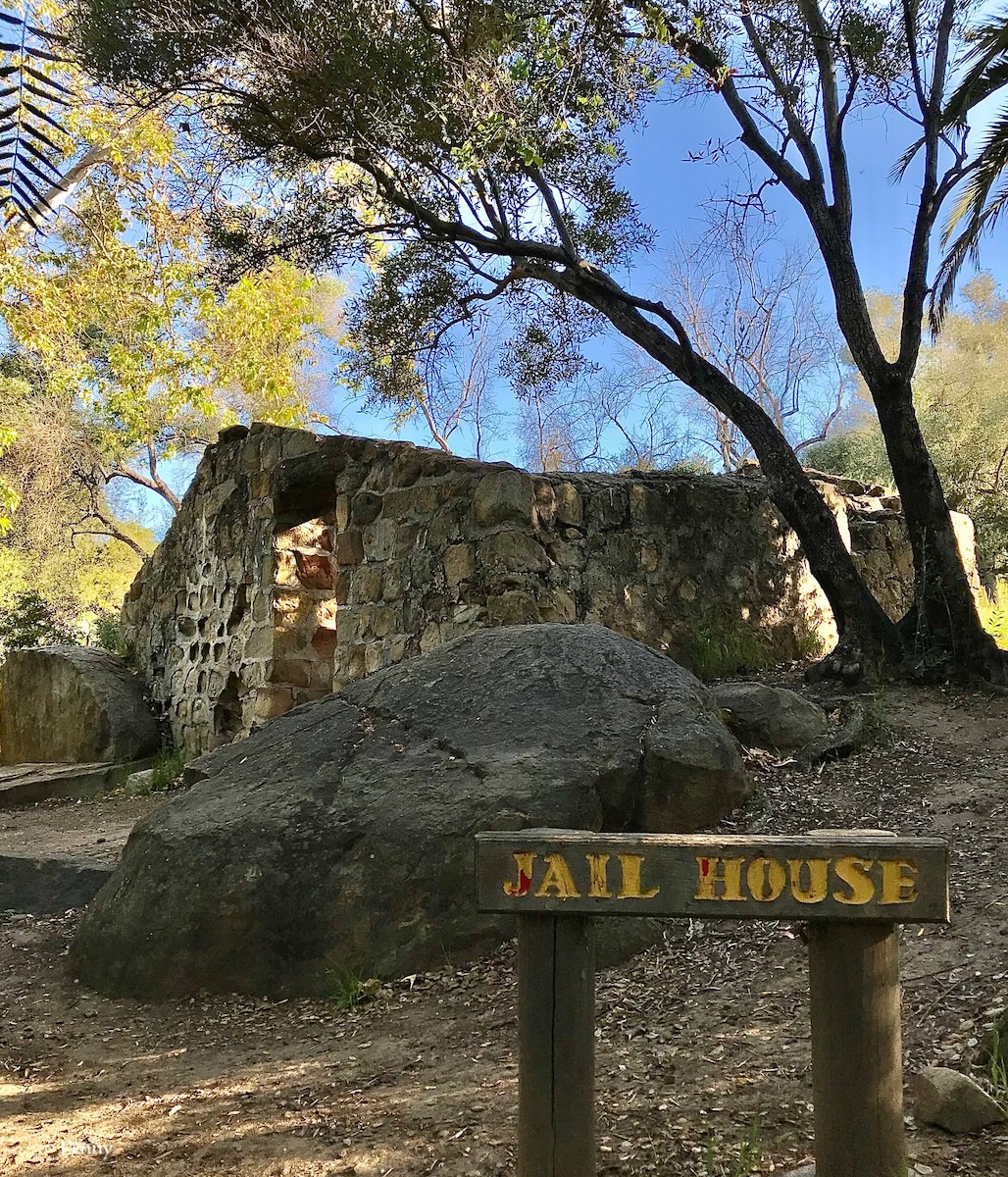 Stone jailhouse built by the Chumash Indians on the mission grounds in Santa Barbara, California. Oak trees in the background. Sign with yellow letters.