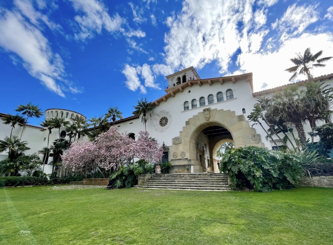 Santa Barbara County courthouse with pink flowers and palm trees on a clear blue day.
