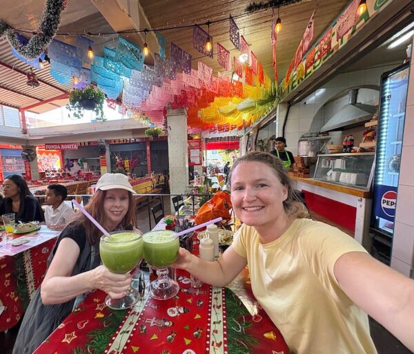 two women holding large glasses of green juice at Mercado Merced, Oaxaca.